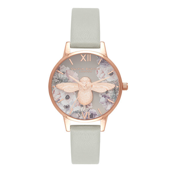 Olivia Burton Watercolour Florals Grey & Rose Gold OB16PP43 damklocka har en rund, grå blommig urtavla prydd med ett stort roséguldfärgad bi i mitten. Indexen och visaren, liksom ramen och boetten, är också roséguldfärgade. Remmen är en grå läderrem utan sömmar.