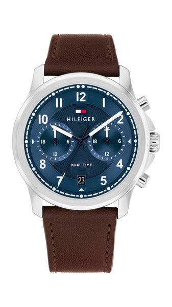 Tommy Hilfiger Wesley TH1710625 Dual Time herrklocka har en rund, blå urtavlan har en dubbel tidsfunktion, en datumvisning, vita index och visare. Ramen och boetten är silverfärgade. Remmen är en brun läderrem med sömmar.