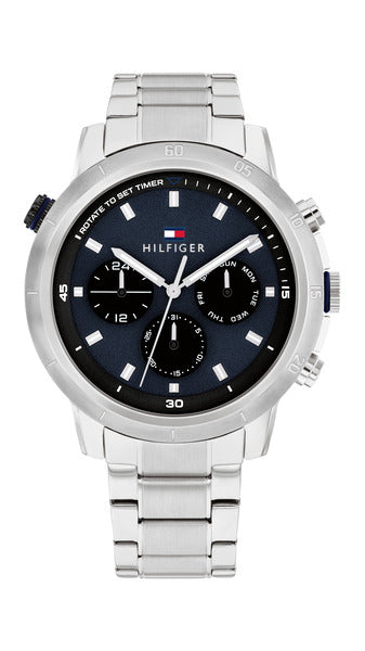Tommy Hilfiger Troy TH1792104 herrklocka har en rund, blå urtavla med datum-, veckodag- och 14/24 h-visning samt silverfärgade självlysande index och visare. Ramen, boetten och remmen är silverfärgade.