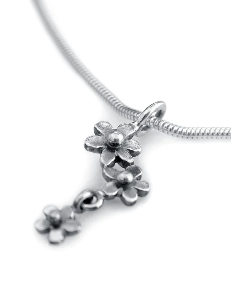 Guldviva Förgät Mig Ej halsband har en tunn silverkedja. Hänget består av tre små blommor, varav den lägsta är något separerad från de andra.