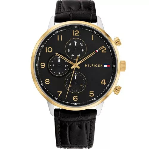 Tommy Hilfiger Leonard TH1791986 herrklocka har en rund, svart urtavla med datum-, veckodag- och 12/24h-visning samt guldfärgade numeriska index och visare, och minutmarkeringar på kanten. Ramen är guldfärgad och boetten är silverfärgad. Remmen är en svart läderrem med svarta sömmar.
