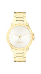Calvin Klein Vivacious CK25100023 damklocka har en rund, silverfärgad urtavla med guldfärgade index och visare. Ramen, boetten och remmen är guldfärgade.