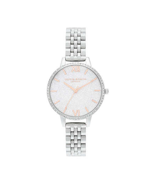 Olivia Burton Whte Demi Glitter OB16GD68 damklocka har en rund, silverfärgad glittrande urtavla med roséguldfärgade index och visare. Ramen, boetten och remmen är silverfärgade. Ramen är dekorerad med strass.