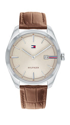 Tommy Hilfiger Theo TH1710430 herrklocka har en rund, beige urtavla med datumvisning samt silverfärgade index och visare. Ramen och boetten är silverfärgade. Remmen är en brun läderrem med bruna sömmar.
