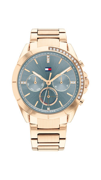 Tommy Hilfiger Kennedy TH1782386 damklocka har en rund, blå urtavla med datum-, veckodag- och 12/24h-visning samt roséguldfärgade index och visare. Ramen, boetten och remmen är roséguldfärgade. Ramen och index är dekorerad med smyckestenar.